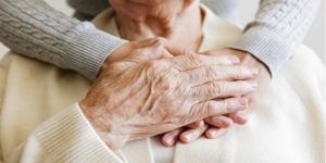 Mature female in an elderly care facility recieves help from a hospital personnel nurse. Senior woman, aged wrinkled skin and hands of her care giver. 